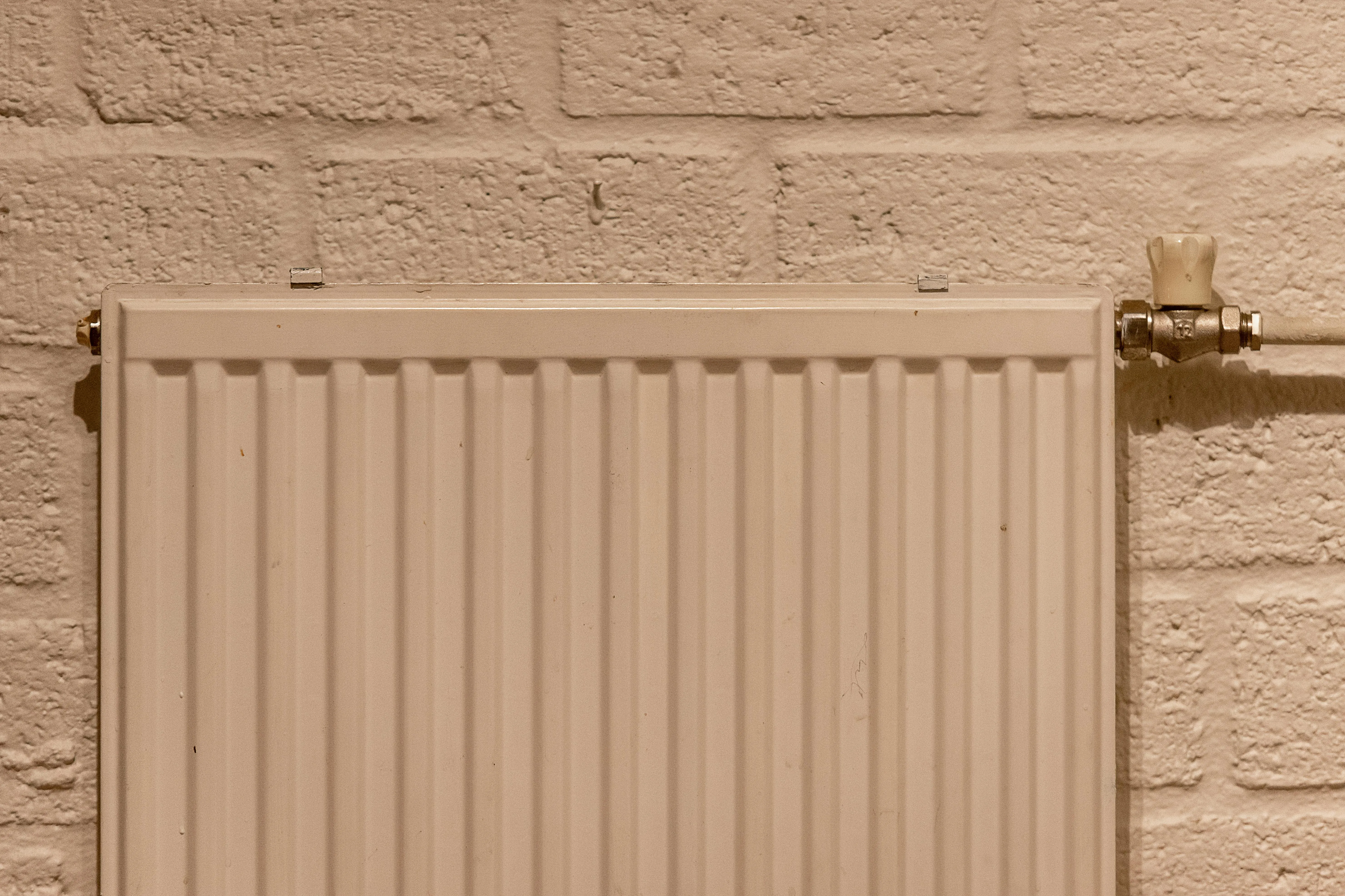 A cream panel radiator against a textured wall in a Leicester home — what you save by switching depends on what currently heats it.